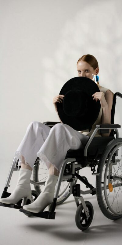Stylish young woman in a wheelchair holding a hat, showcasing disability and fashion.