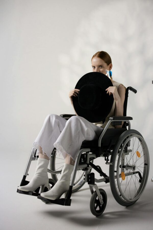 Stylish young woman in a wheelchair holding a hat, showcasing disability and fashion.