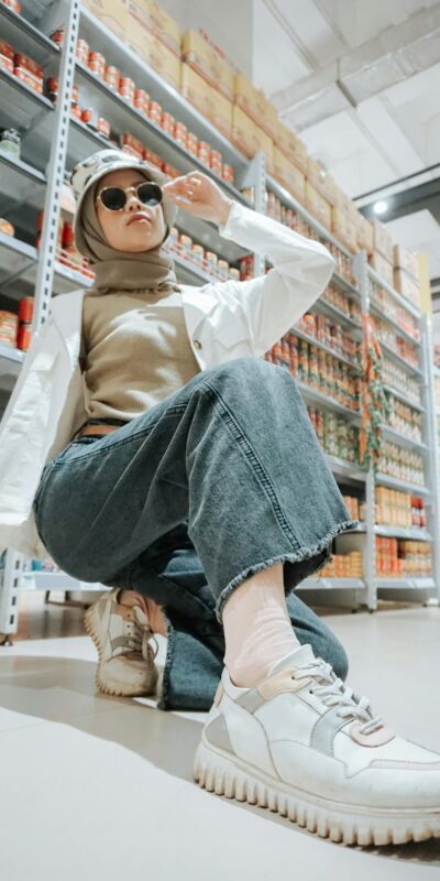 Woman in a hijab and casual outfit poses confidently in a shopping aisle.