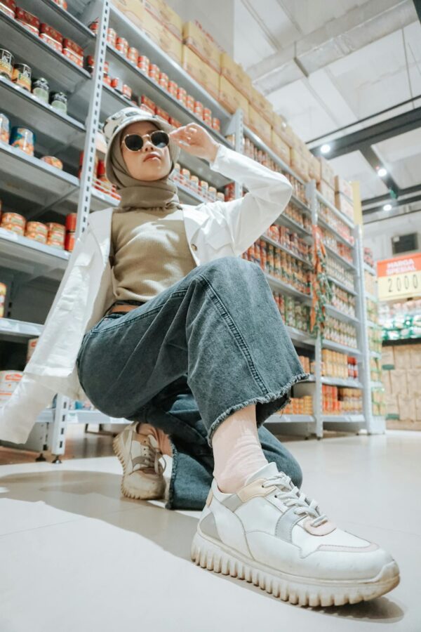 Woman in a hijab and casual outfit poses confidently in a shopping aisle.