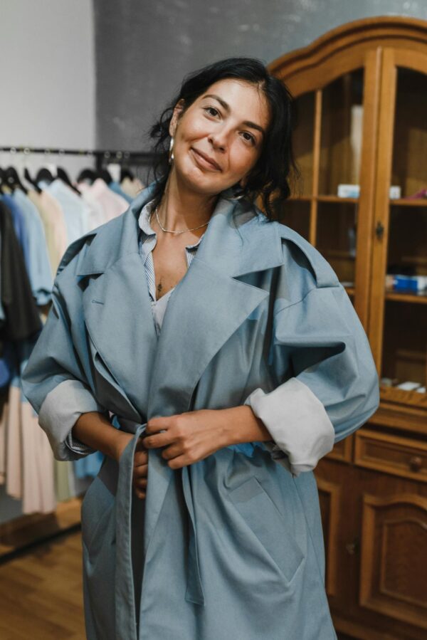 Woman in a stylish blue trench coat shopping in a trendy boutique. Indoor setting, fashion-focused.